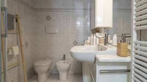 A bathroom with a toilet, bidet, and a sink with toiletries.