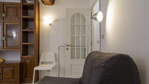 A room with a dark quilted sofa, a white chair, wooden cabinets, and a white door with a glass panel.