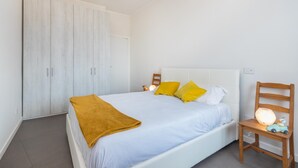 A bedroom with a bed, a wardrobe, a chair, and a nightstand with a lamp.