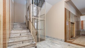 A marble staircase with a red carpet, a metal railing, and a beige wall.