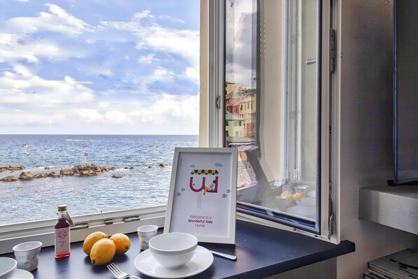 A table with a bottle, lemons, and bowls by a window overlooking the sea.