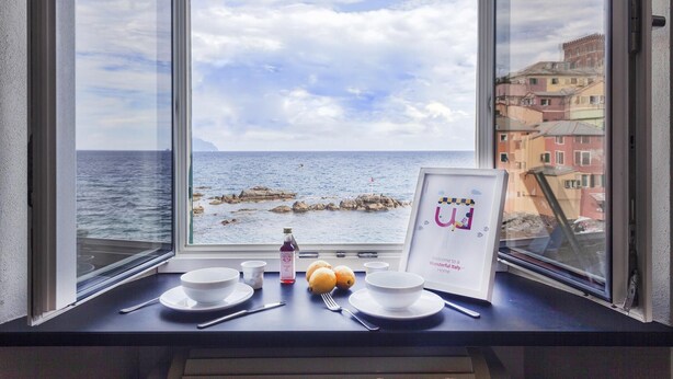 Una mesa con dos cuencos, una botella y un cartel de bienvenida enmarcado junto a una ventana con vistas al mar.