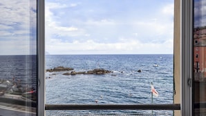 Vista costera a través de una ventana, con afloramientos rocosos, mar tranquilo y una bandera.