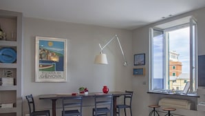 Una sala de estar moderna con comedor, un ventanal con vistas a edificios, un cuadro enmarcado de un río y un televisor.