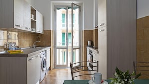 Een compacte keuken met een wasmachine, een eettafel met kop en schotel, en uitzicht op het balkon.