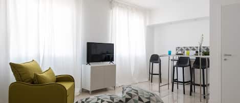 A modern living room with a sofa, a TV, and a dining area with chairs and a table.
