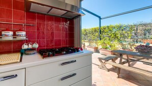 A kitchen with red tiles, a gas stove, and a window overlooking a garden.