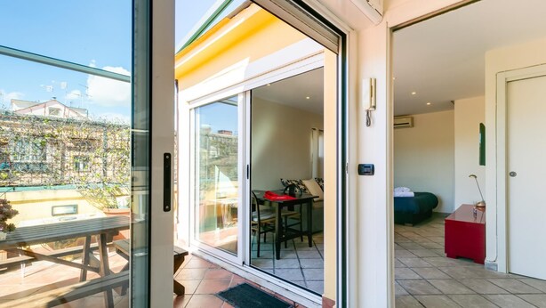 A modern apartment with a sliding glass door leading to a balcony, a dining area, and a bedroom.