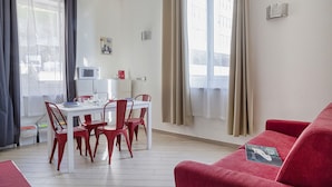 Ett modernt vardagsrum med en röd soffa, en matplats med ett vitt bord och röda stolar samt stora fönster med gardiner.
