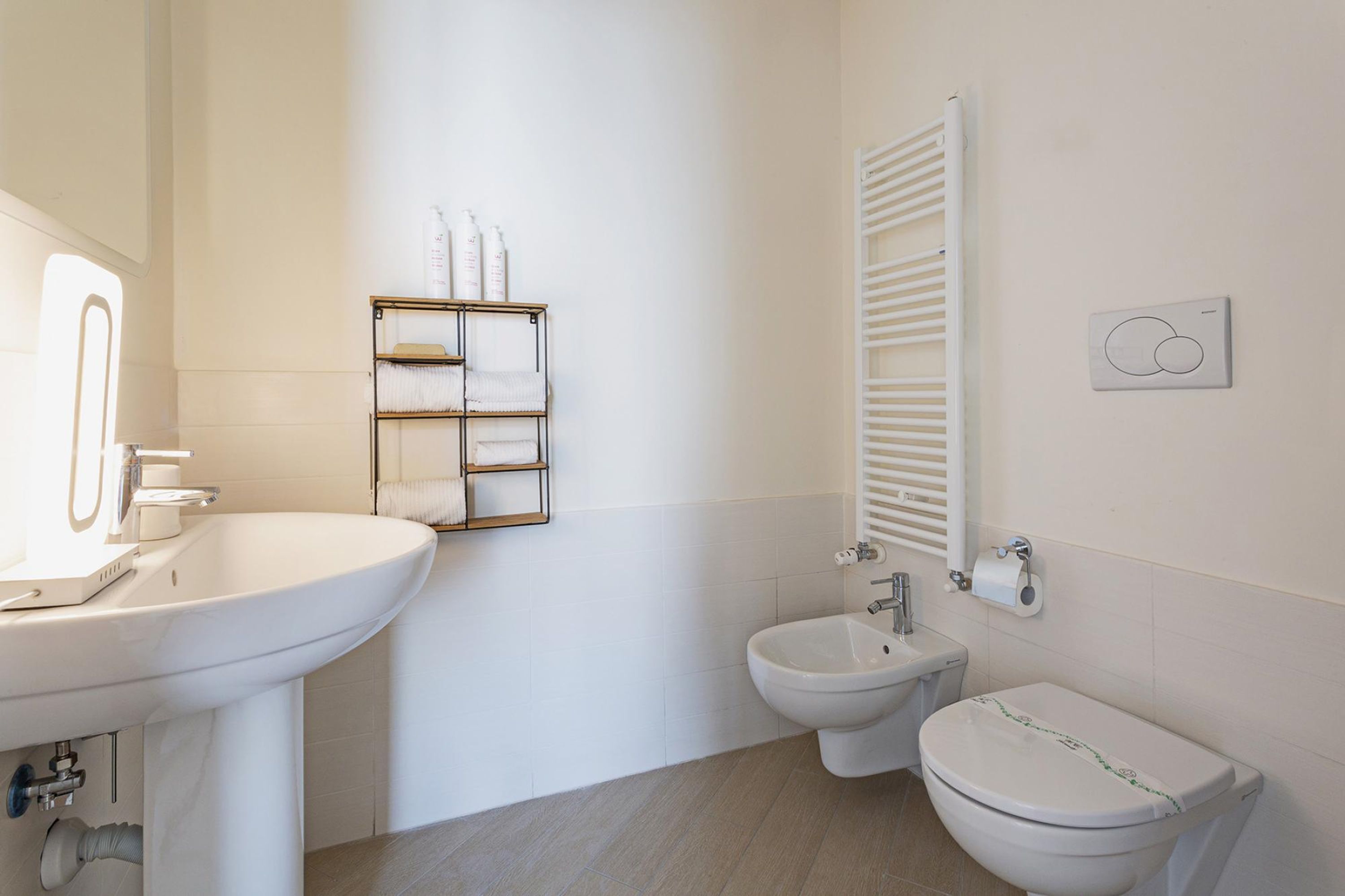 Een moderne badkamer met een wit wastafel, bidet en toilet, een handdoekhouder en een radiator.