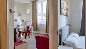 Ett hotellrum med en säng, en matplats med ett bord och stolar samt ett fönster med gardiner.