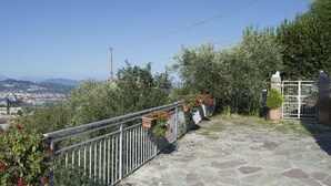 Una terraza empedrada con barandilla de metal, plantas en macetas y vistas a un paisaje urbano al fondo.