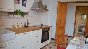 Una cocina con armarios blancos, encimera de madera, estufa y comedor con una mesa para dos.