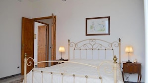 Un dormitorio con una cama, dos lámparas de noche, una puerta de madera, un cuadro enmarcado en la pared y una alfombra estampada.