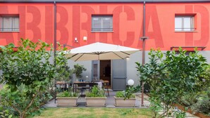 An outdoor patio area with a table and chairs under a large umbrella, surrounded by potted plants and a fence. - Casa con Giardino all ex Fabbrica di Pomodoro by Wonderful Italy (Palermo)