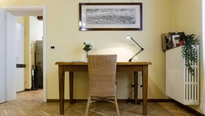 A room with a wooden desk, wicker chair, a framed map on the wall, a radiator, and a potted plant. - Casa Garisenda by Wonderful Italy (Bologna)