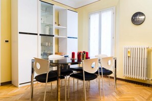 Un coin repas avec une table et des chaises, un meuble vitré contenant de l’ustensile de cuisine, un radiateur et une horloge murale.