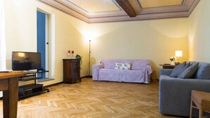 A living room with a television, a sofa, a grey armchair, a wooden cabinet, and a floor lamp. - Casa Garisenda by Wonderful Italy (Bologna)