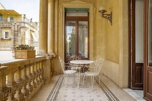 A balcony with a white metal table and chairs, a potted plant, and a view of the street. - Cavour Apartment With Balcony by Wonderful Italy (Noto)