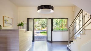 Ein Hotel-Rezeptionsbereich mit einem Holzbüro, einer großen Pendelleuchte und Blick auf den Garten durch eine Glastür.