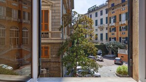 Vista dalla finestra su una strada con auto parcheggiate e palazzi.