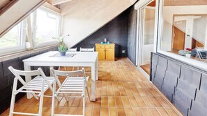 Een eethoek met een witte tafel en stoelen, een klein kastje en een raam met een plant op de tafel.