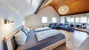 Een moderne slaapkamer met een groot bed, een bank en een eethoek, met veel natuurlijk licht.