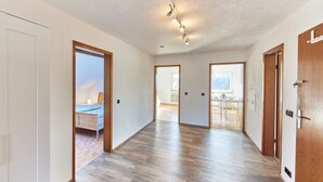 Een ruime gang met houten vloeren en witte wanden, die leidt naar een slaapkamer met een bed en een klein tafeltje.