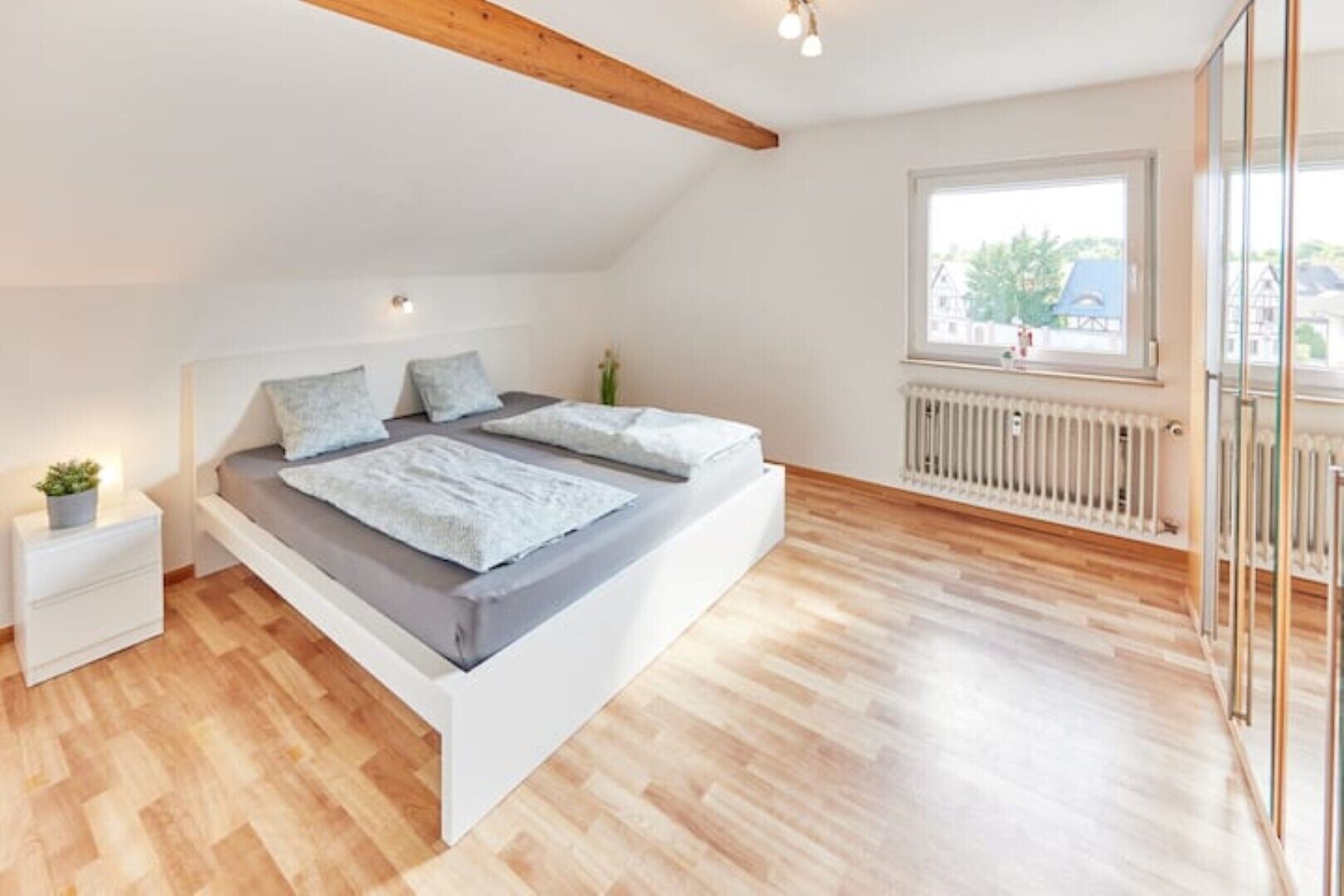 Ein modernes Schlafzimmer mit Schlafbox, weißen Wänden, Holzboden und einem Fenster mit Blick auf Gebäude.