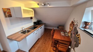 A compact kitchen with white cabinets, a wooden countertop, a sink, a coffee maker, and a dining table with chairs.