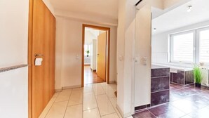 A hallway with a wooden door, a white door, and a window with a plant.