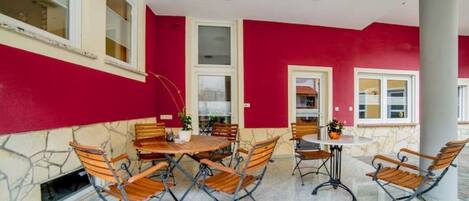 An outdoor patio with a red wall, stone flooring, and metal-framed wooden tables and chairs.