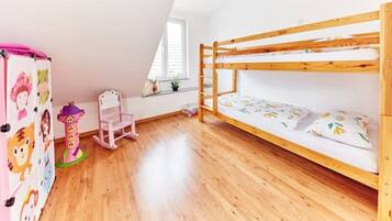 Ein Kinderzimmer mit Etagenbett, Holzboden, einem rosa Stuhl und einer Wand mit Zeichentrickfiguren.