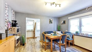 Ein Essbereich mit Holztisch und Stühlen, eine Küchenzeile mit Geräten sowie ein Fenster mit Blick.