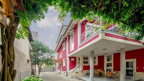 Ein rotes Gebäude mit Balkon, einem gepflasterten Innenhof und einem Baum.