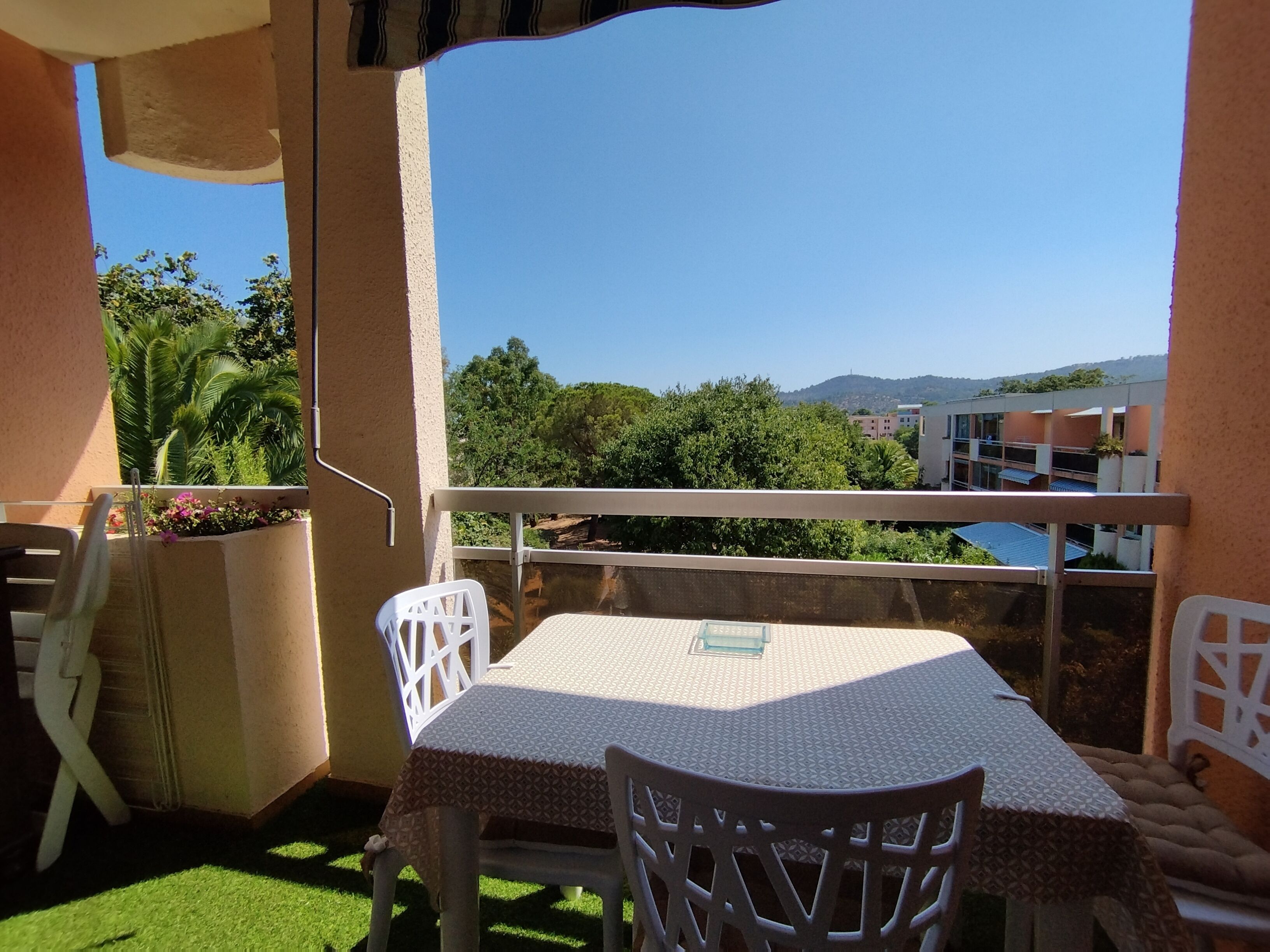 Un balcon avec une table et des chaises, offrant une vue panoramique sur les arbres et les bâtiments.
