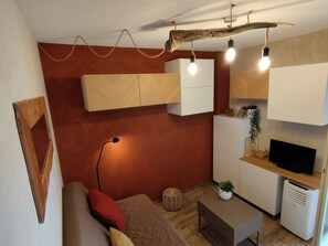 Een gezellige, compacte leefruimte met een bank, een salontafel, een televisie en een kitchenette.