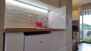 A compact kitchen with white tiles, a wooden countertop, a built-in dishwasher, and a red dish rack.