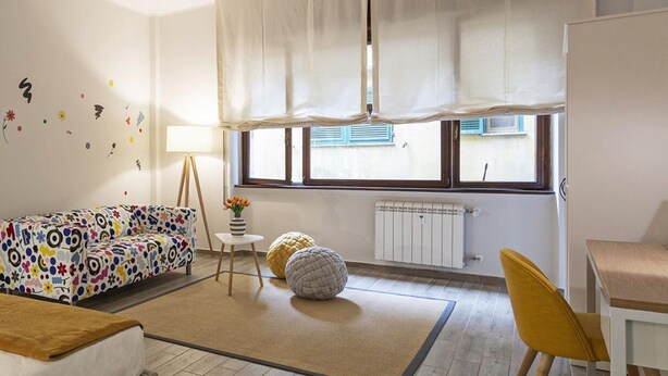 Una sala de estar moderna con un sofá, un sillón amarillo, una mesita con un florero y una ventana con cortinas.