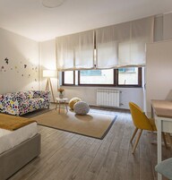 Una sala de estar moderna con un sofá, un sillón amarillo, una mesita con un florero y una ventana con cortinas.