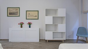 Una habitación con un armario blanco, dos cuadros enmarcados, una silla azul y un estante blanco.