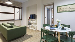 Una sala de estar moderna con un sofá verde, una mesa de comedor con sillas, un televisor y una estantería.
