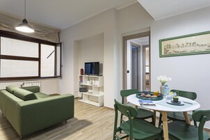 Una sala de estar moderna con un sofá verde, una mesa de comedor con sillas, un televisor y una estantería.