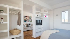 Un dormitorio moderno con cama, televisor, sofá y estanterías empotradas.