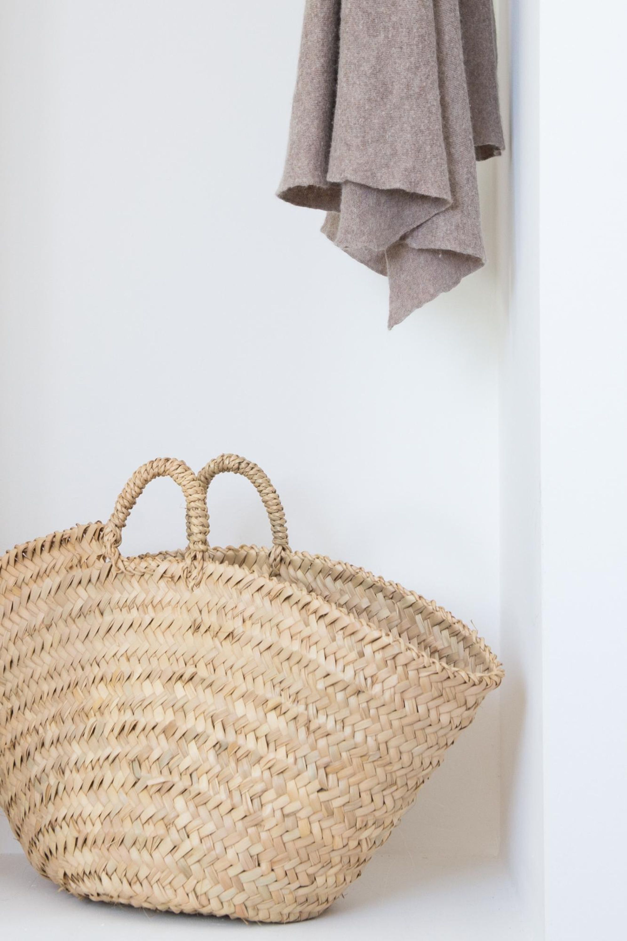 A woven basket with handles against a white wall.