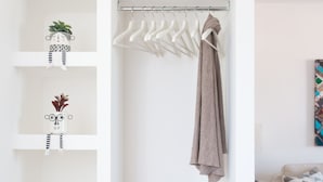 Un armario blanco con estantes, una barra para colgar ropa y una cesta tejida.