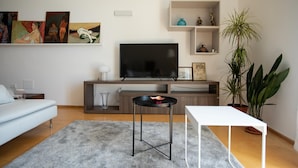 Ett modernt vardagsrum med en platt-TV, en vit soffa, ett soffbord och en krukväxt.