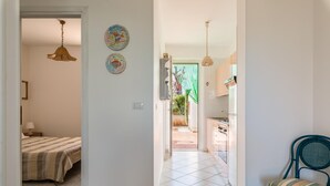 A room with a bed, a chair, and a kitchen area visible through an open door. - White Sea - Villetta Ariel (Carovigno)