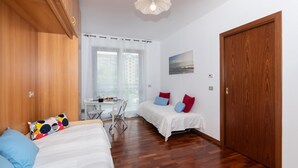 Una habitación con dos camas, un armario de madera, una mesa de comedor con sillas y una ventana con cortinas.