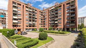 Un edificio residencial de varios pisos con balcones, un patio empedrado y zonas verdes circundantes.